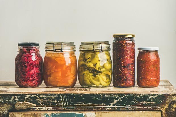 Őszi szezonális fermentált zöldség üvegekbe helyezve egy sorban a rusztikus konyhai fiók fölött, fehér háttér, másol hely, szögletes termés. Őszi otthoni ételkonzervek vagy konzervek